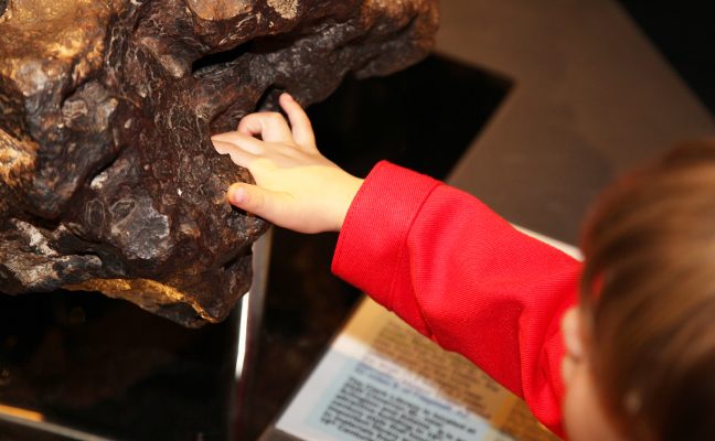 child touching meteorite on display