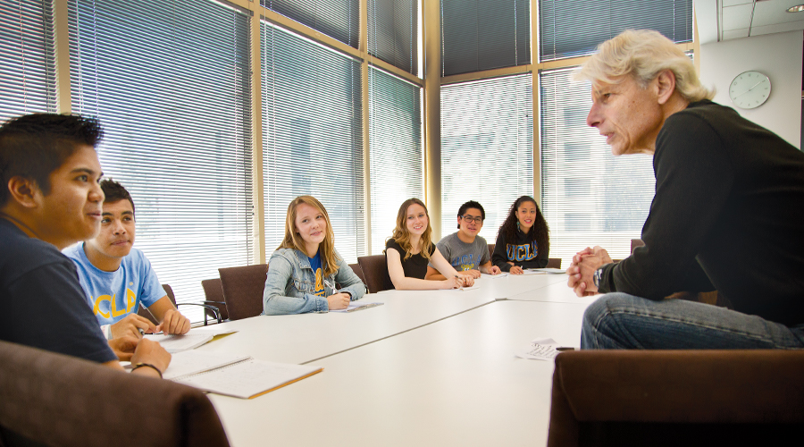 male professor in discussion with students seated around table
