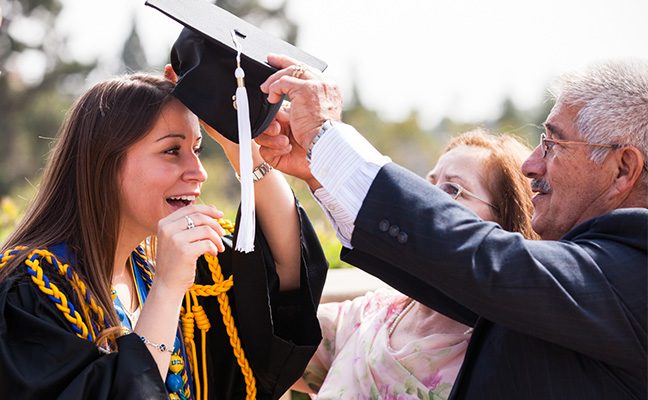 Father placing mortarboard on head of young woman in gown