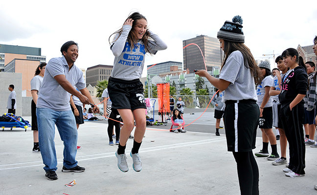 Girl jump roping on blacktop with man and student.