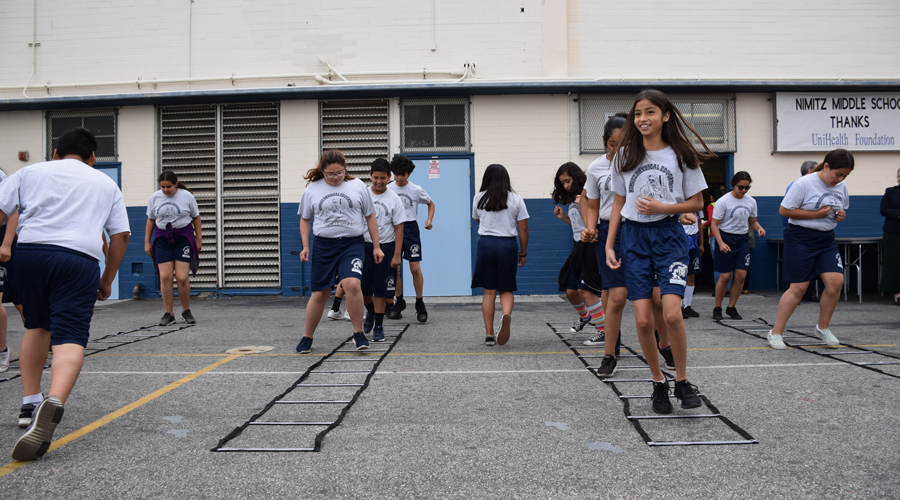 Students outdoors performing drills with exercise ladders.