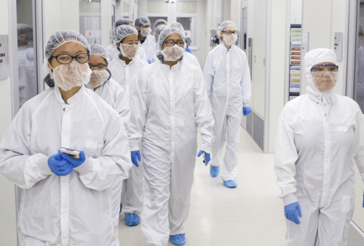 A group of students in white safety overalls walking into a cleanroom of a laboratory.