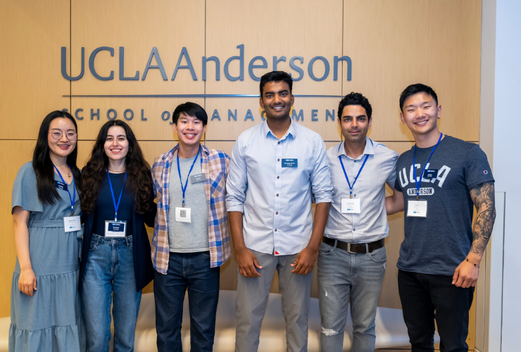 A group of UCLA Anderson students smiling and posing together in front of the UCLA Anderson School of Management sign.