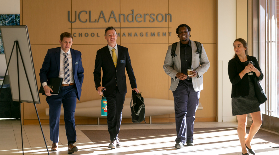 4 UCLA Anderson students walk confidently down a hallway, with the UCLA Anderson School of Management sign behind them.